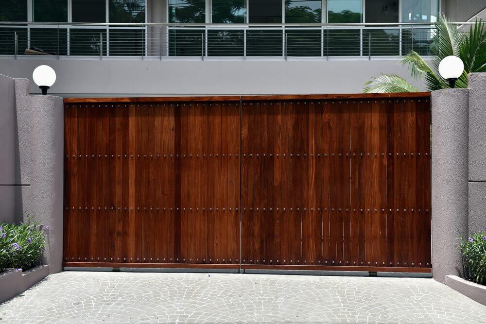 a large dark brown wooden automatic gate with rendered walls either side